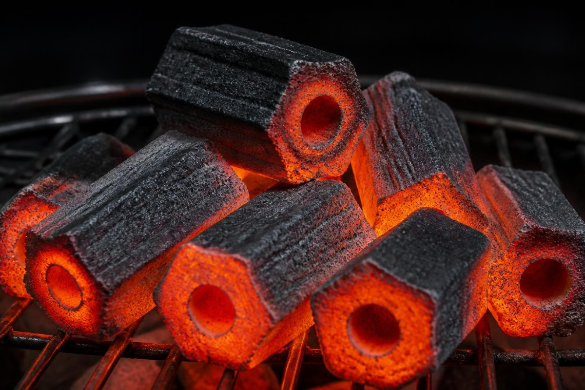 Premium glowing binder free sawdust charcoal briquettes with central hollow design on a commercial grill.